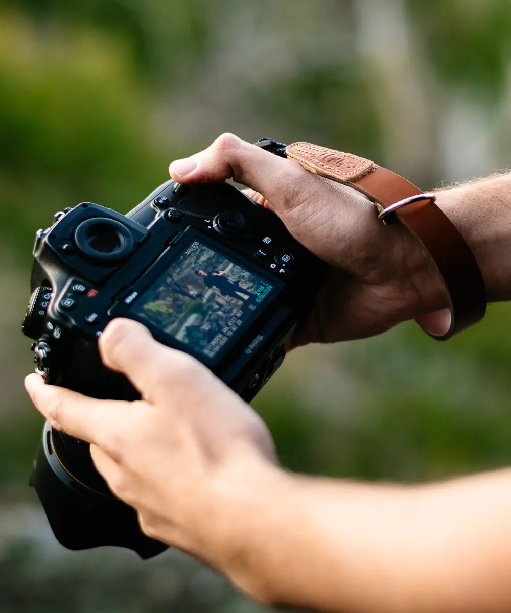 Photographer holding camera with leather lucky camera strap in tan
